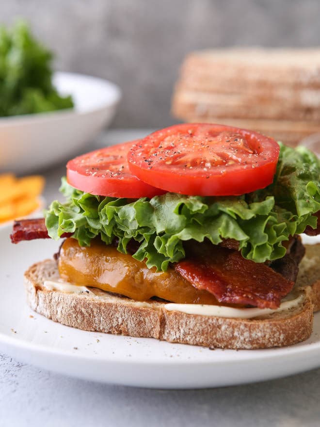 Cheeseburger topped with bacon, lettuce, and tomato served on toasted white bread