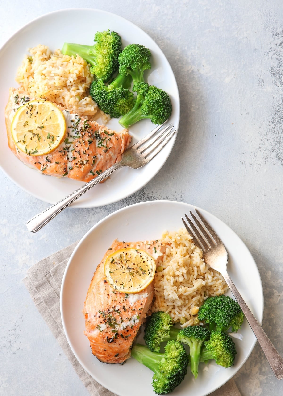 Baked salmon with lemon, rice pilaf, and broccoli on two plates set for a date night dinner.