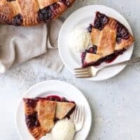slices of cranberry blueberry pie on plates with vanilla ice cream