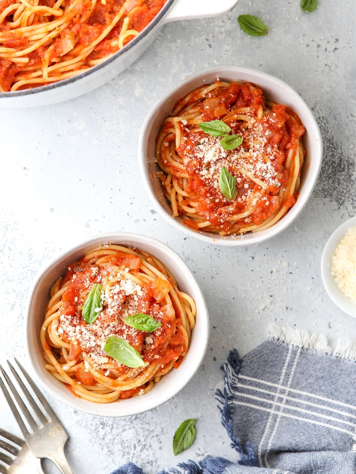 Bowls of spaghetti with homemade marinara sauce, topped with cheese and basil.