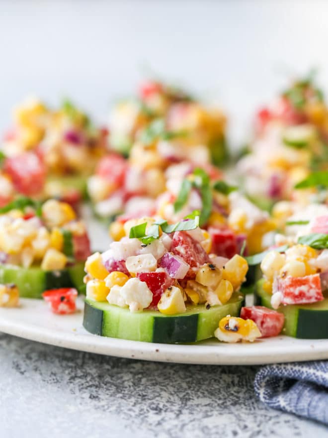 Individual cucumber bites topped with a corn and red pepper salad filled with feta, basil, and a creamy dressing.
