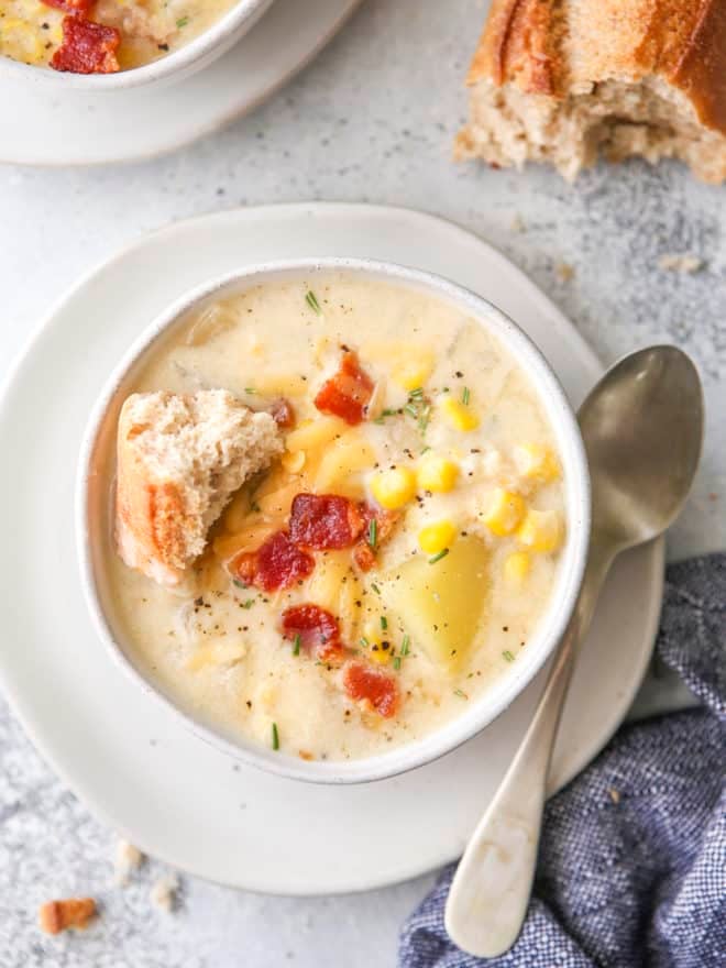 close up of cheesy corn chowder in a bowl with a baguette