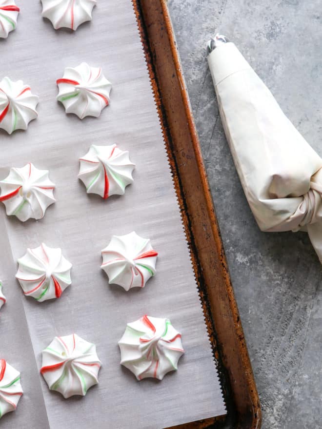 piped meringues on a sheet pan with piping bag