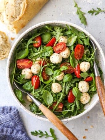 arugula caprese salad in a bowl with bread on the side