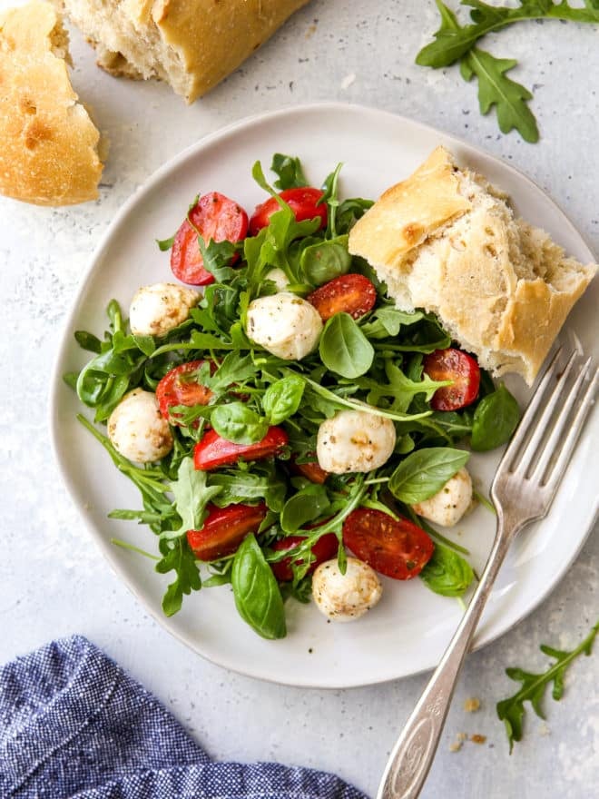 arugula caprese salad on a plate with a slice of bread