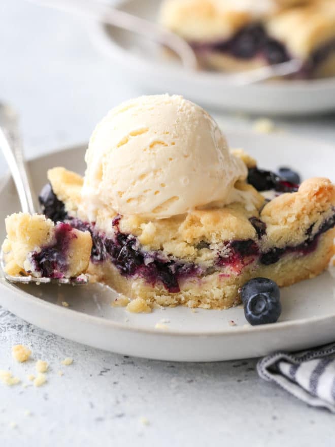 blueberry pie bars with a scoop of ice cream on a plate, bite taken out