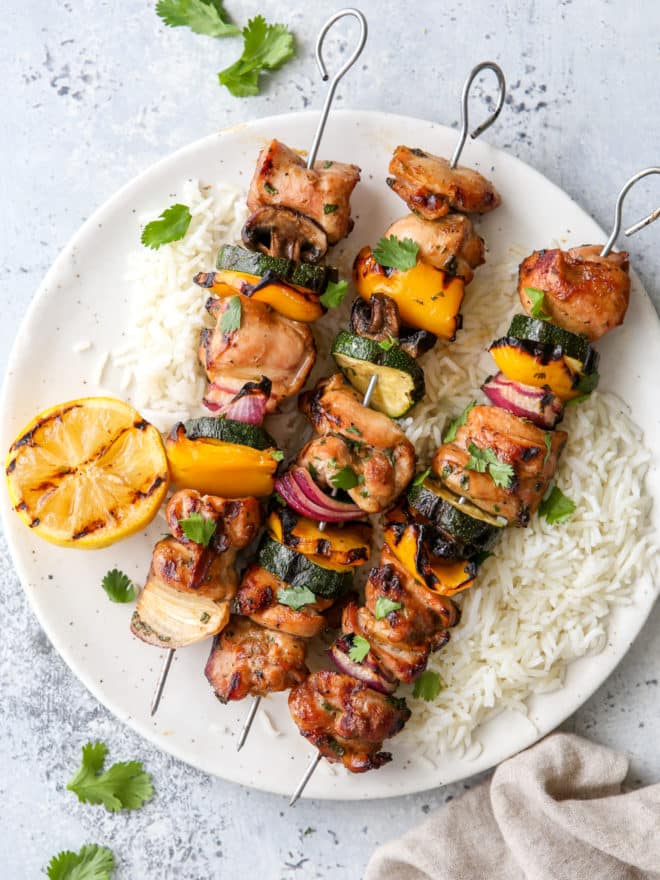 grilled lemon-cilantro veggie skewers on a plate with rice underneath