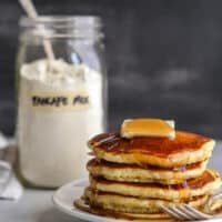 stack of pancakes on a plate with jar of buttermilk pancake mix in background
