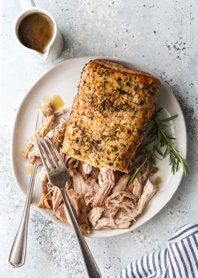 slow cooker rosemary balsamic pork roast shredded on a plate with gravy on the side