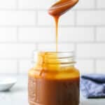 pouring a spoonful of homemade caramel sauce into a jar