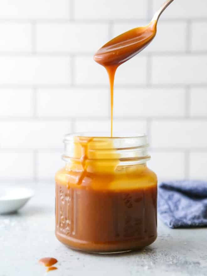 pouring a spoonful of homemade caramel sauce into a jar