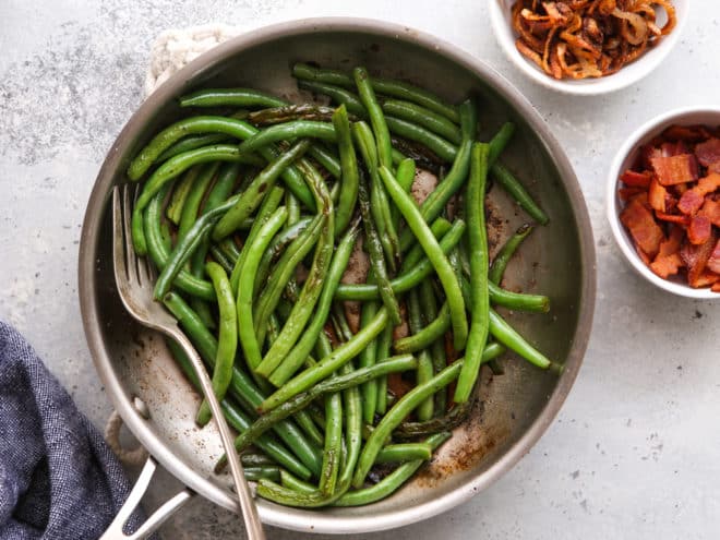 sauteed green beans in pan with bacon and shallots on side