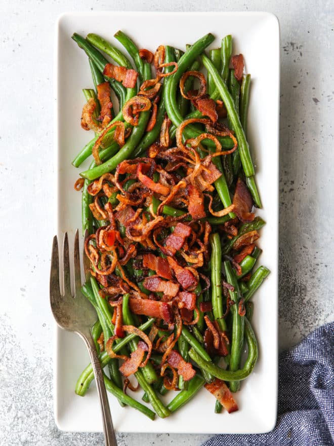 green beans with crispy shallots and bacon on a platter with fork