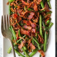 closeup of green beans with crispy shallots and bacon on a platter with fork
