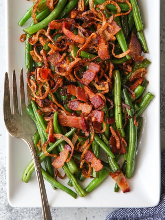 closeup of green beans with crispy shallots and bacon on a platter with fork