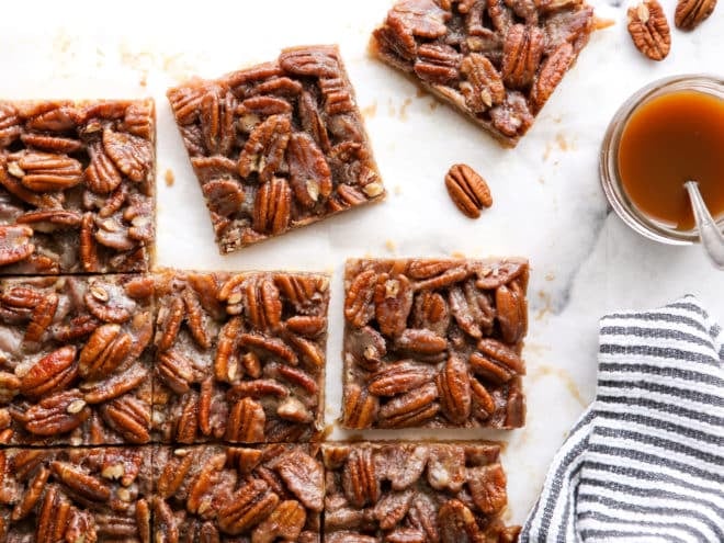 pecan pie bars cut into squares with jar of caramel