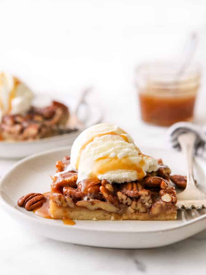 closeup of pecan pie bar with ice cream and caramel drizzle on a plate
