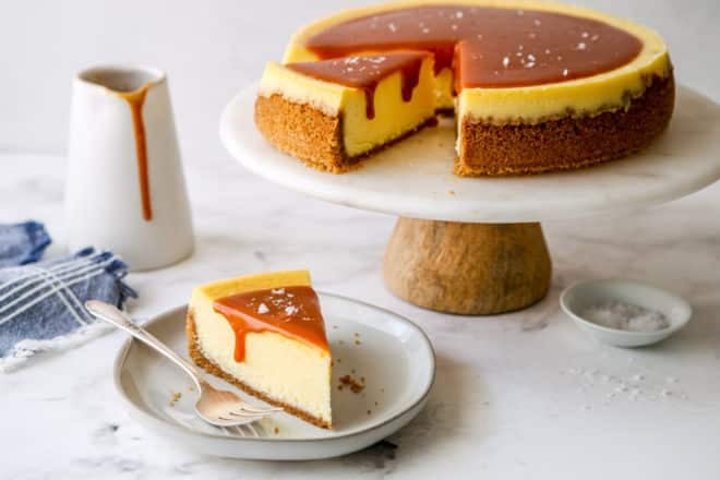 slice of salted caramel cheesecake on a plate with cake stand in background