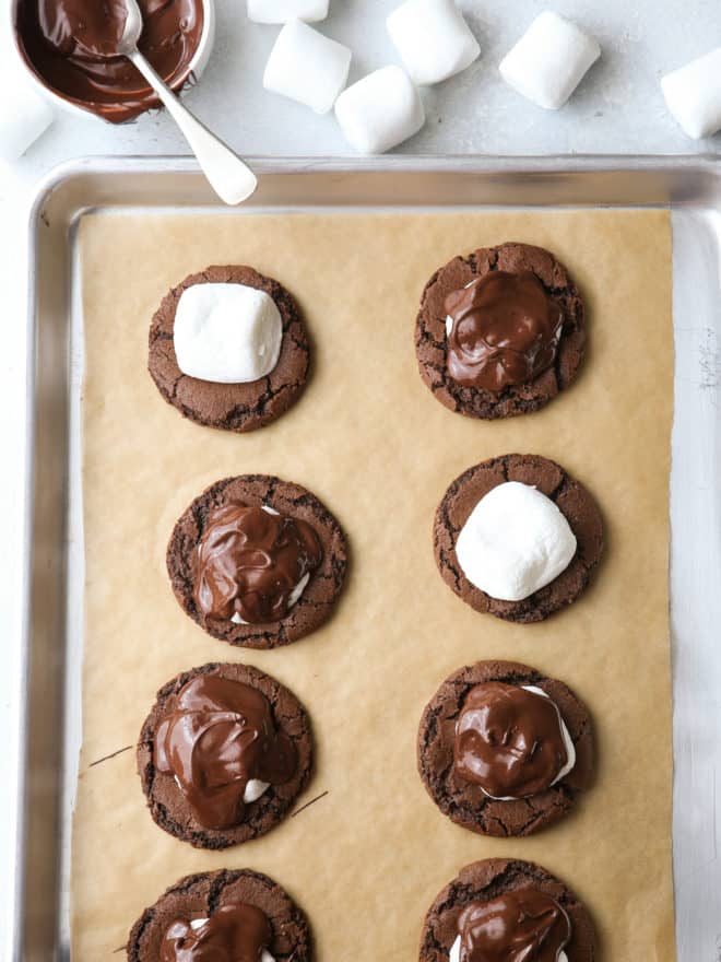 Adding marshmallows and chocolate to chocolate cookies on a sheet pan