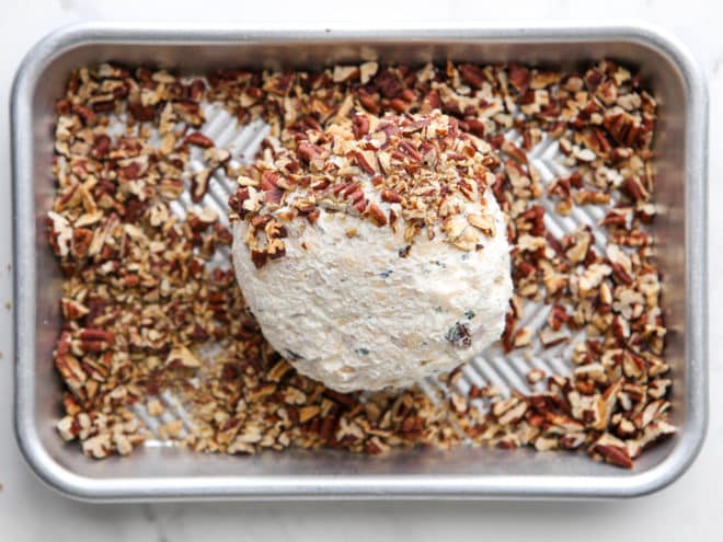 covering cheeseball with chopped pecans