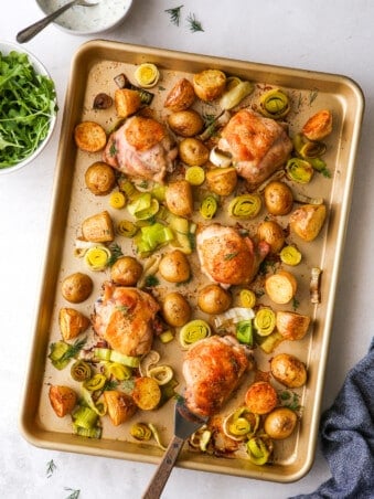 one-pan roasted chicken and potatoes with bowl of arugula and yogurt dill sauce