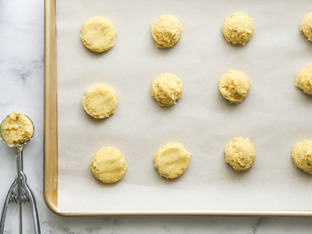 cookie scoop with lime cornmeal cookie dough on sheet pan