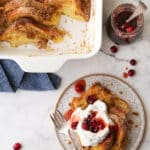 baked french toast on a plate with whipped cream and cranberry maple syrup