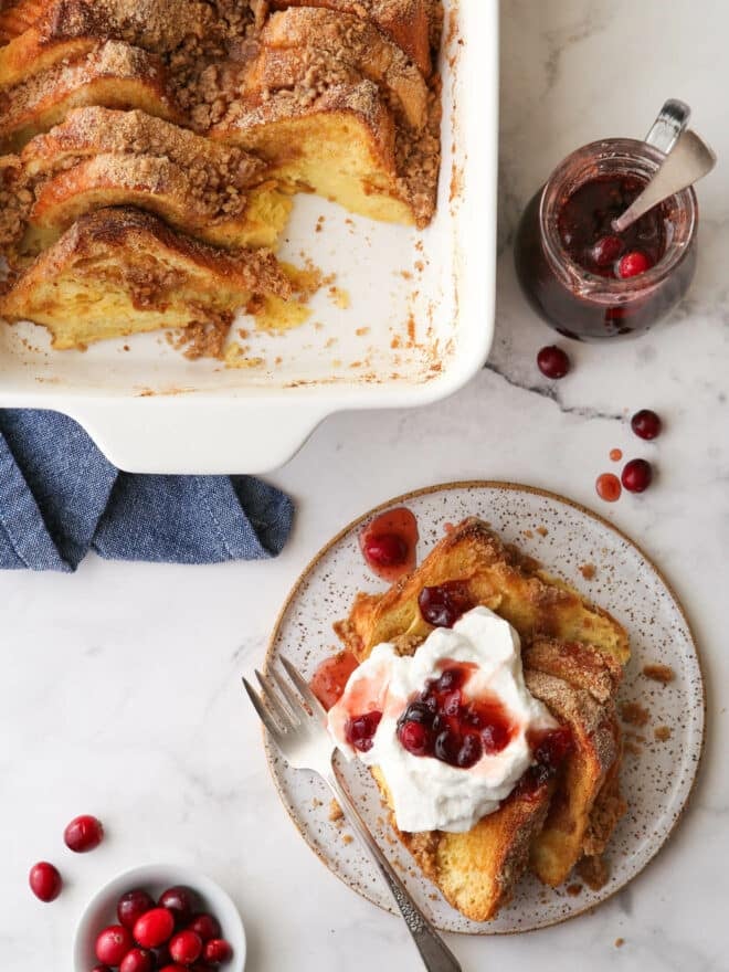 baked french toast on a plate with whipped cream and cranberry maple syrup