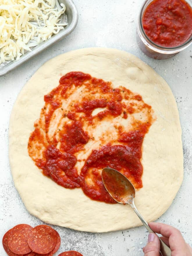 spreading pizza sauce on pizza dough