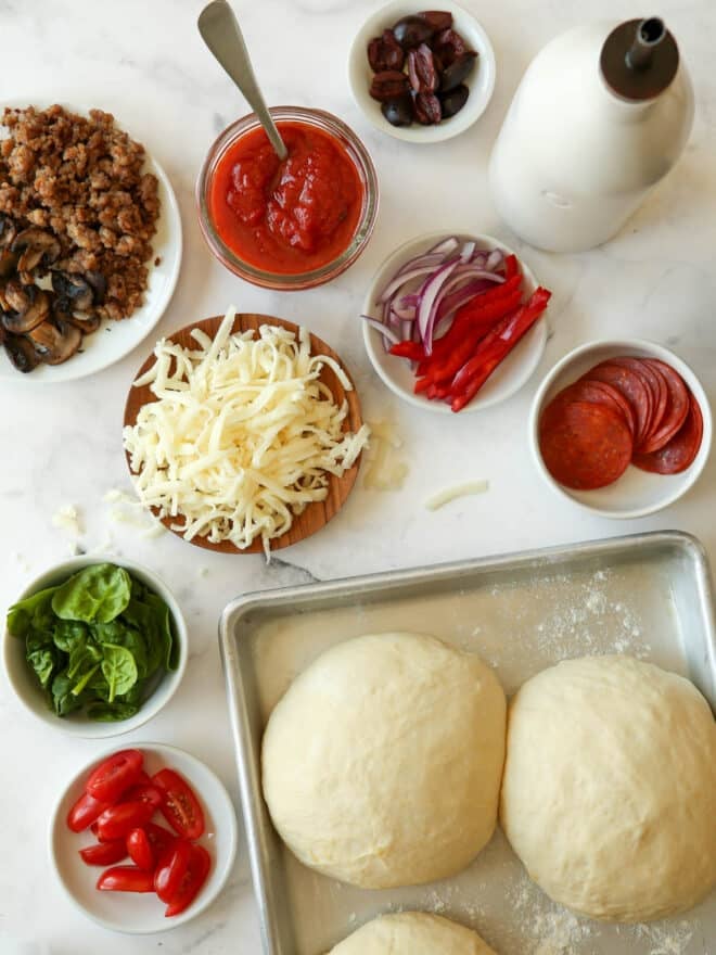 pizza dough and pizza toppings measured out and prepped on counter
