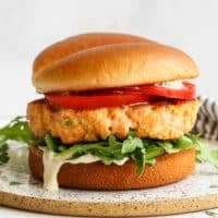A salmon burger dressed with tomatoes, dressing, and arugula.